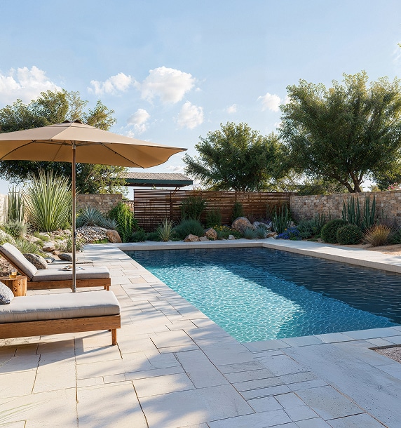 Piscine rectangulaire, chaises longues et parasol beige sur terrasse carrelée claire. Jardin désertique luxuriant, mur de pierre et ciel bleu.